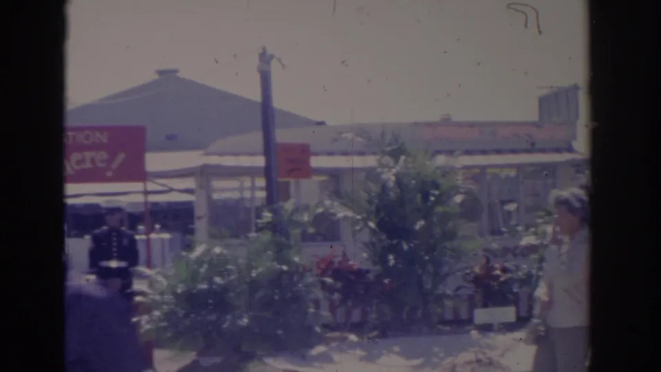 1962 Florida fairground view with visitors walking near planted displays, vendor structures, and partially visible signs.