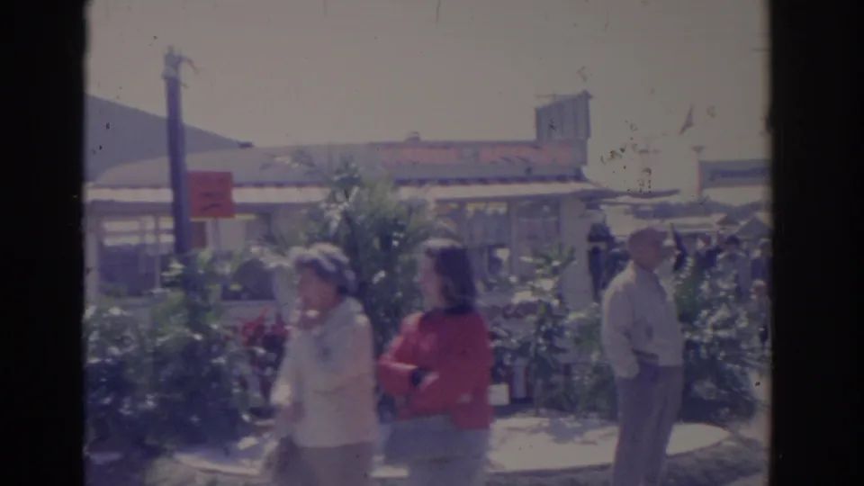 1962 Florida home-movie frame of fairgoers, including two women in the foreground, moving through a landscaped fairground area.
