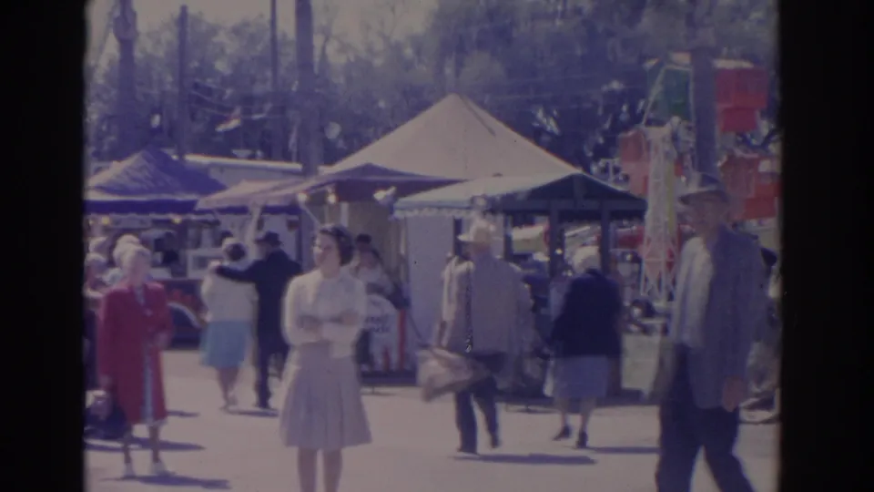 1962 Florida carnival scene with fairgoers, canvas tents, vendor counters, flags, and a red amusement structure at the right edge.