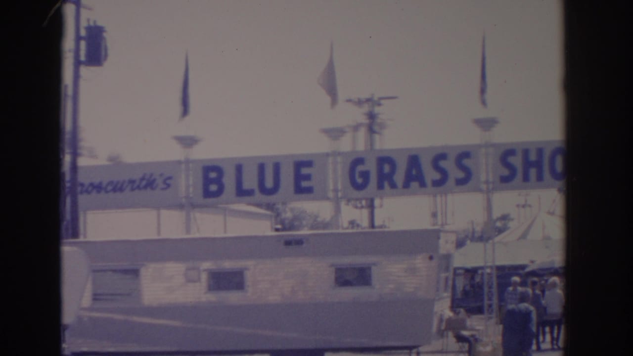 1962 Florida fairground view with the Blue Grass Shows sign over a trailer and a small group of visitors near the entrance.