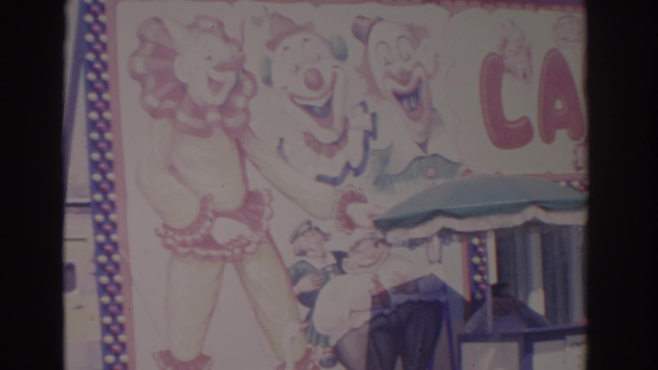 1962 Florida home-movie frame with the Laughterland sign partly visible, showing clown artwork, red lettering, and a booth canopy.