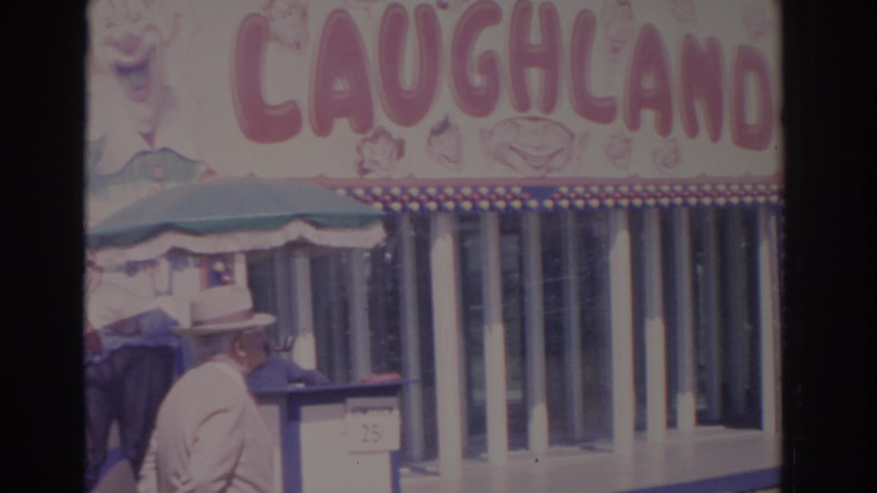 Suited man in a hat passing a Laughland carnival entrance.