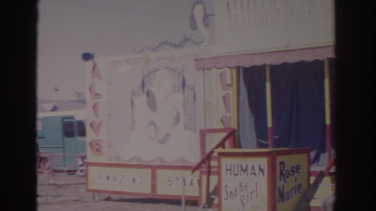 1962 Florida 8mm frame showing the Human Snake Girl carnival booth with red steps, blue curtains, and hand-painted signage.