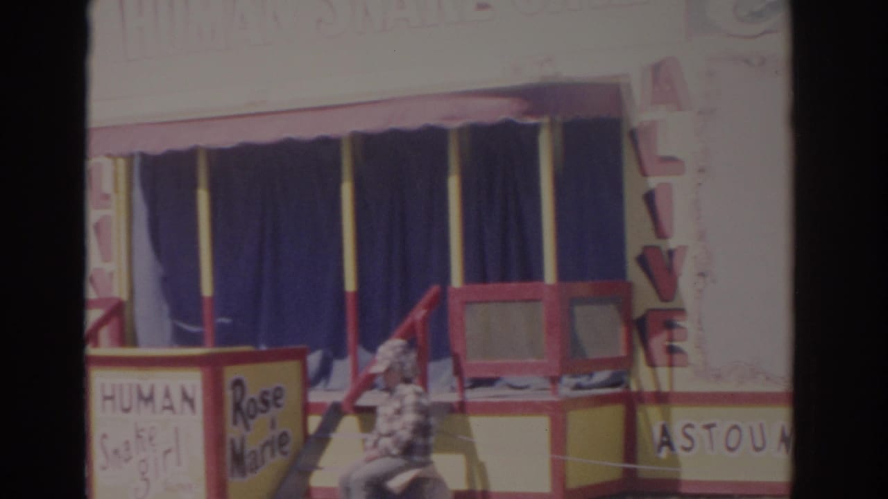 Carnival booth with Human Snake Girl and Rose Marie signs beside a red and yellow entrance.