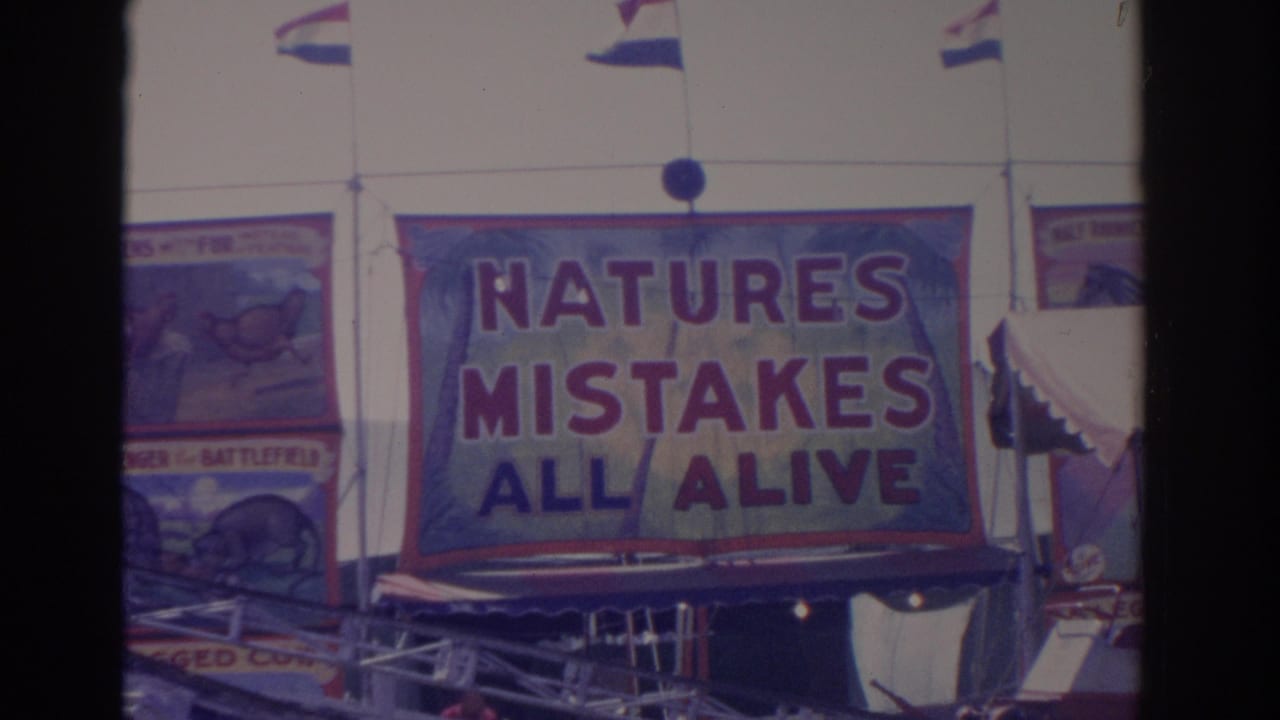 1962 Florida 8mm frame showing a large red and blue carnival banner reading NATURES MISTAKES ALL ALIVE with flags above.