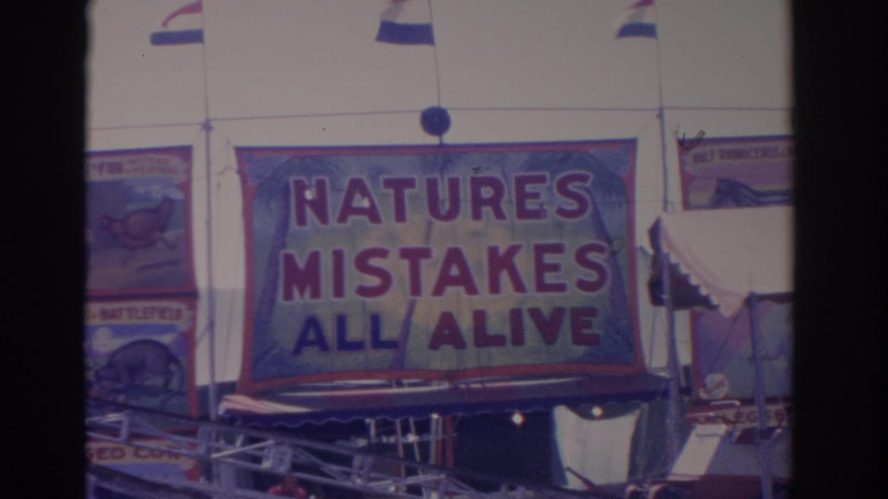 The home-movie frame centers on the NATURES MISTAKES ALL ALIVE sideshow banner, with flags and adjacent painted signs visible.
