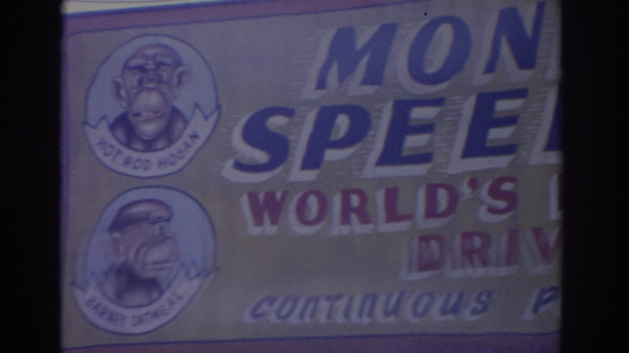 Florida 1962 frame showing a close, cropped view of a monkey-themed carnival banner with painted portraits and partial words.