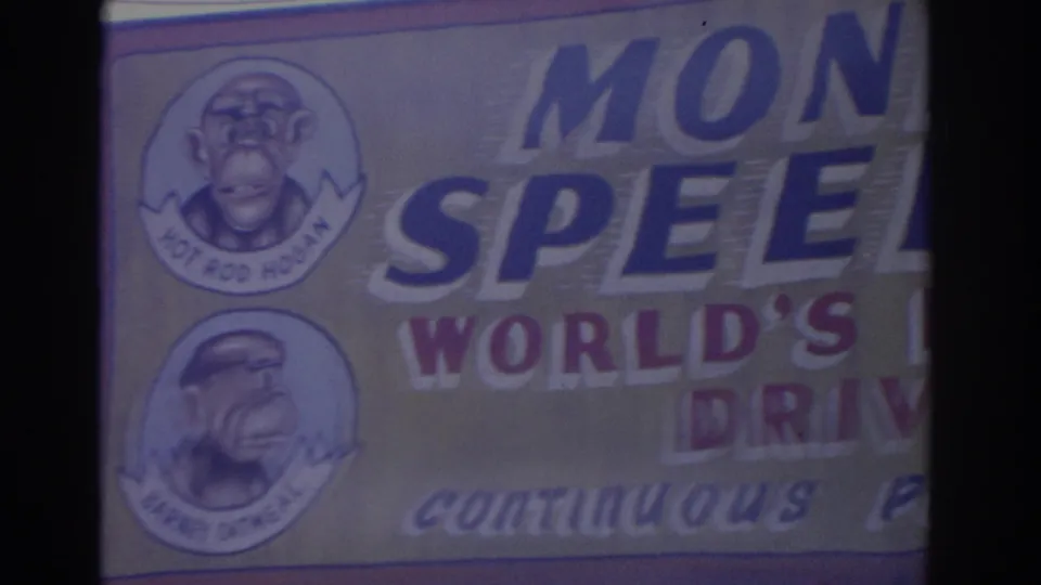 Florida 1962 frame showing a close, cropped view of a monkey-themed carnival banner with painted portraits and partial words.
