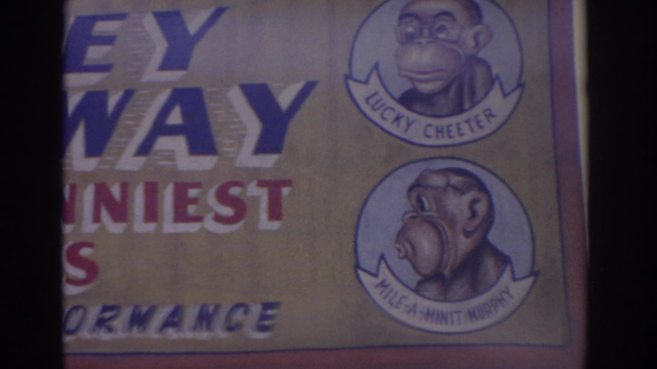 1962 Florida home-movie frame showing a carnival sign with cartoon monkey performer portraits and partial show lettering.