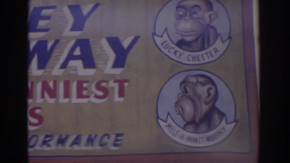 1962 Florida home-movie frame showing a carnival sign with cartoon monkey performer portraits and partial show lettering.