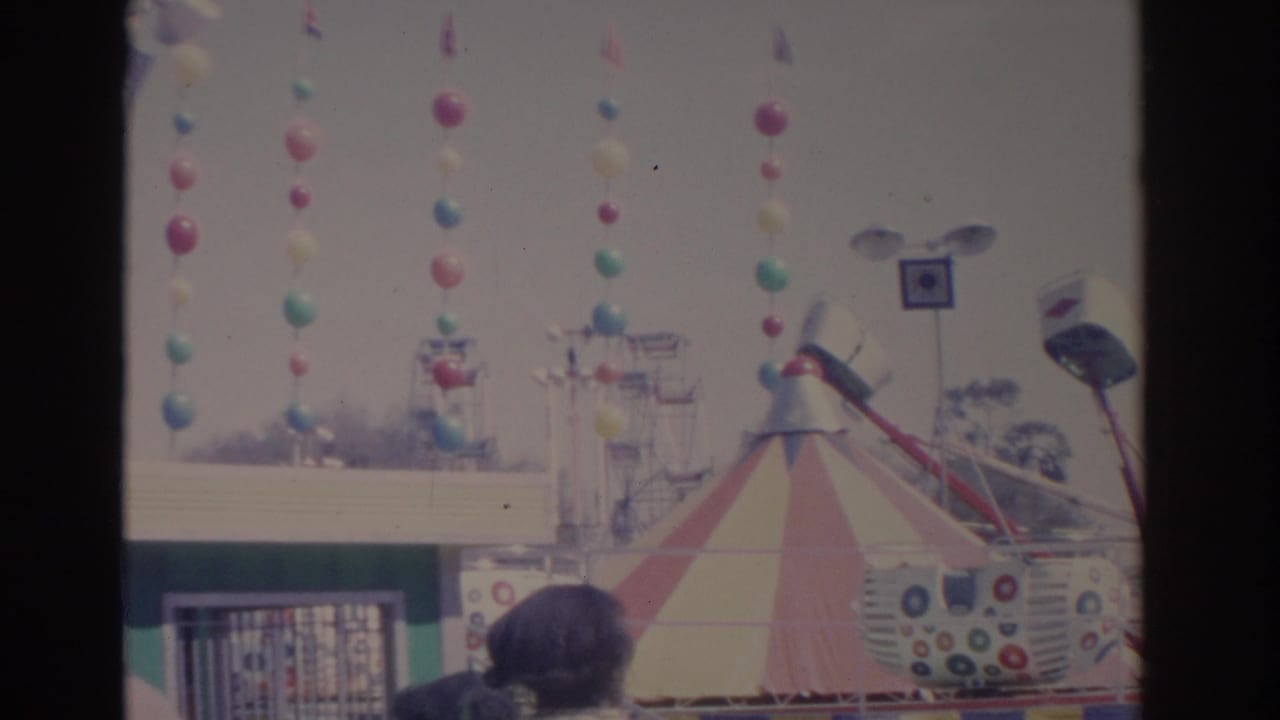 1962 Florida carnival scene with balloon garlands, a striped tent, and amusement ride structures in bright daylight.