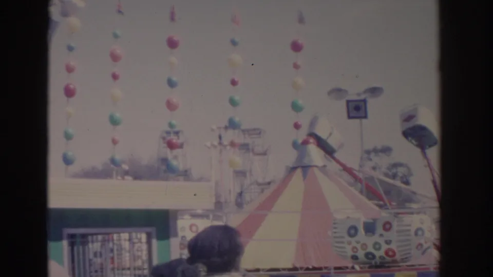 1962 Florida carnival scene with balloon garlands, a striped tent, and amusement ride structures in bright daylight.