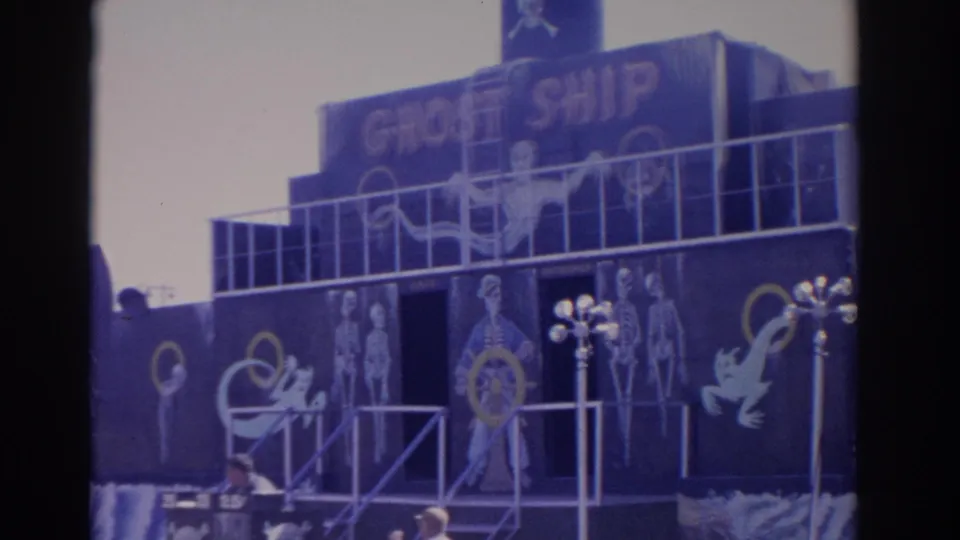1962 Florida 8mm frame showing a Ghost Ship carnival facade with skeleton figures, ghost graphics, railings, and visitor heads at the bottom.