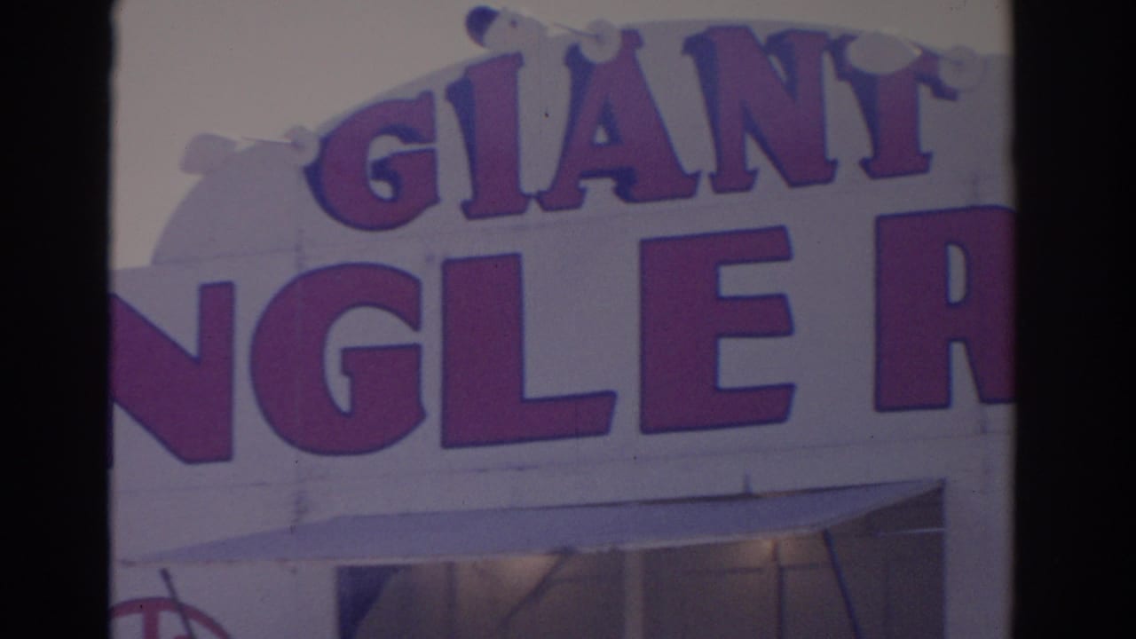 1962 Florida 8mm frame showing close-up purple GIANT lettering and partial storefront sign text on a white commercial facade.