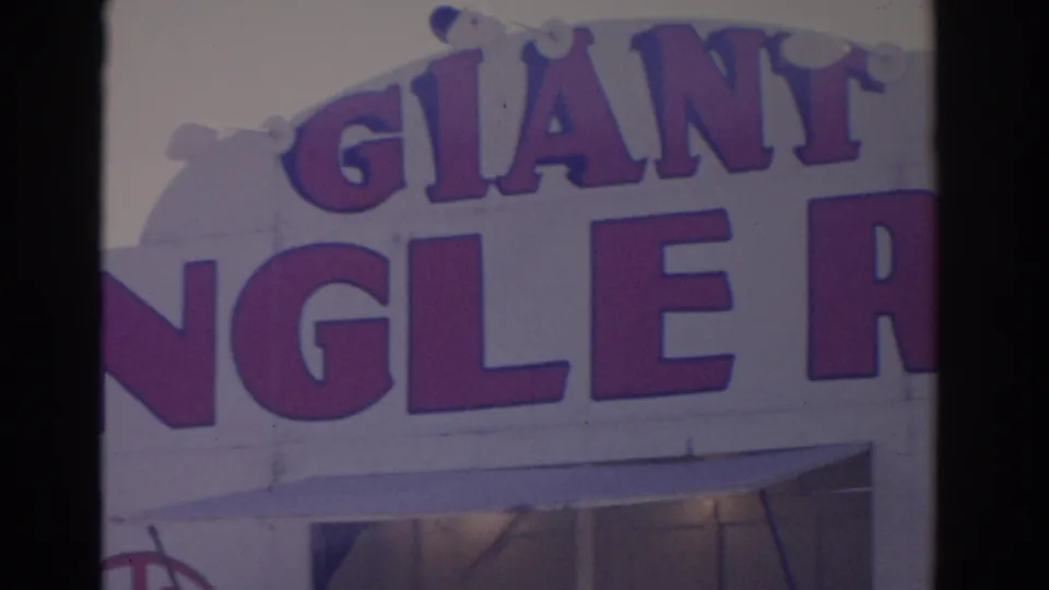 1962 Florida 8mm frame showing close-up purple GIANT lettering and partial storefront sign text on a white commercial facade.