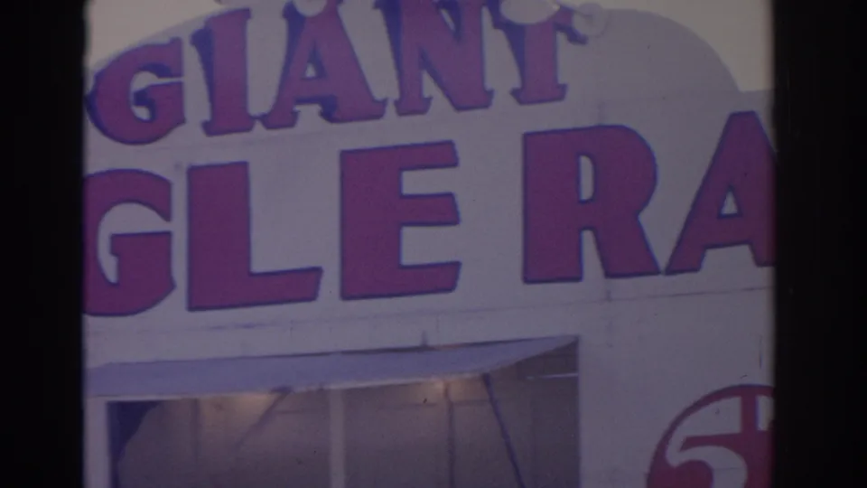 1962 Florida 8mm frame with bold purple facade lettering, including GIANT and partial GLE RA text, on a white storefront exterior.