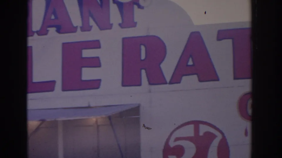 1962 Florida 8mm frame showing partial purple facade lettering, storefront windows, and a circular 57 mark near the lower right.