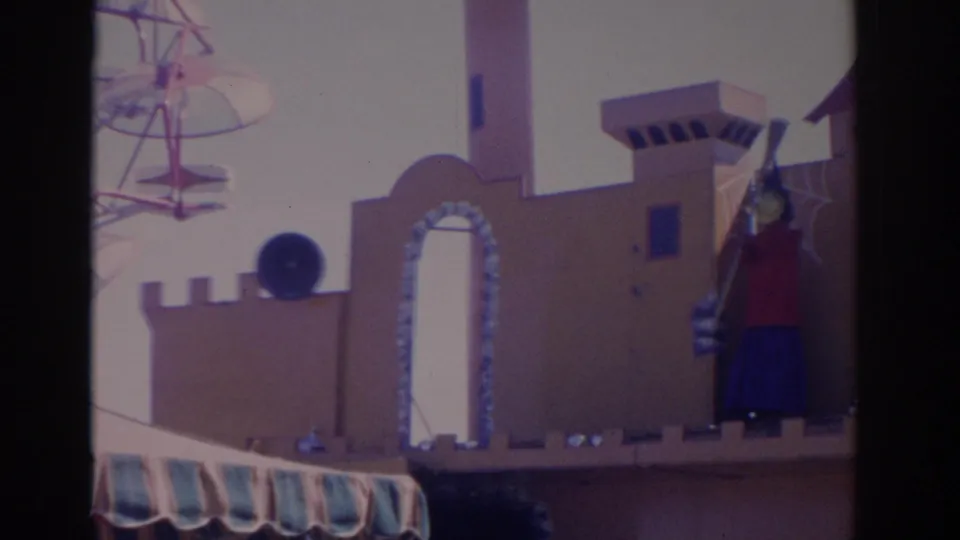1962 Florida amusement park frame showing a castle-like facade, scarecrow figure, and Ferris wheel structure in the background.