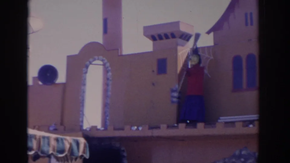 1962 Florida home-movie view of a castle-like amusement structure with an arched doorway and scarecrow figure in bright sun.