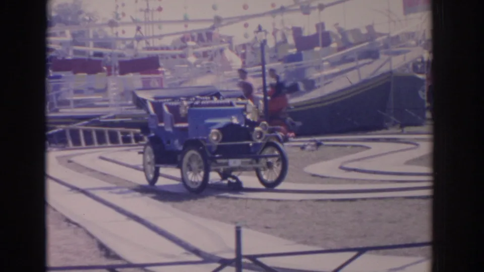 1962 Florida 8mm frame showing a blue antique-style amusement ride car on a curving track with railings and ride structures in the background.
