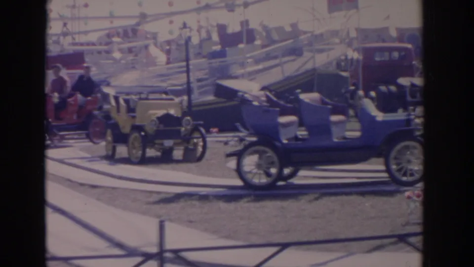 1962 Florida amusement ride frame with yellow and blue antique-style cars carrying visible passengers on a winding track.