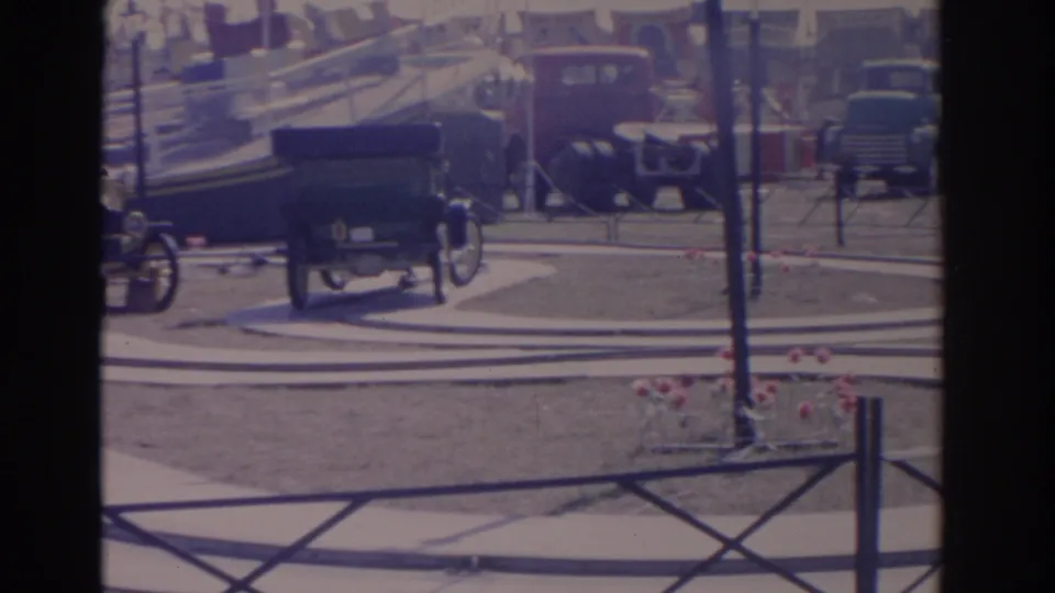 1962 Florida 8mm frame with the rear of an antique-style amusement car moving away on a curved track near planters and railings.