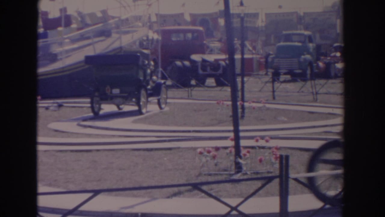 Antique cars parked and moving around a circular outdoor display area.