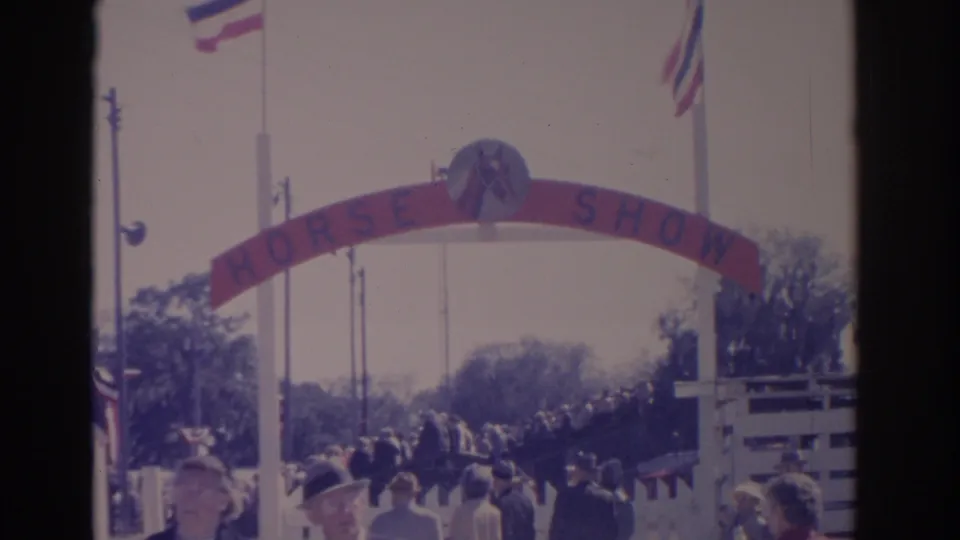 1962 Florida home-movie view of the HORSE SHOW arch, flags, trees, and a crowd moving through or waiting near the entrance.