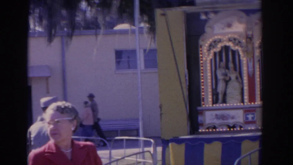 At the 1962 Florida fair, a foreground woman and railings lead toward an ornate illuminated attraction partly entering frame.
