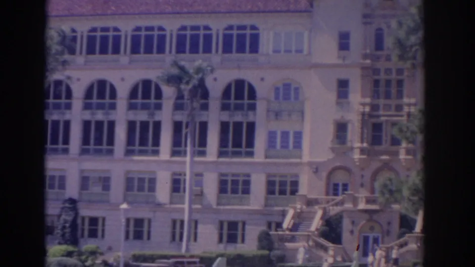 1962 Florida 8mm frame showing the cream building with arched windows, palm trees, shutters, and exterior steps at right.