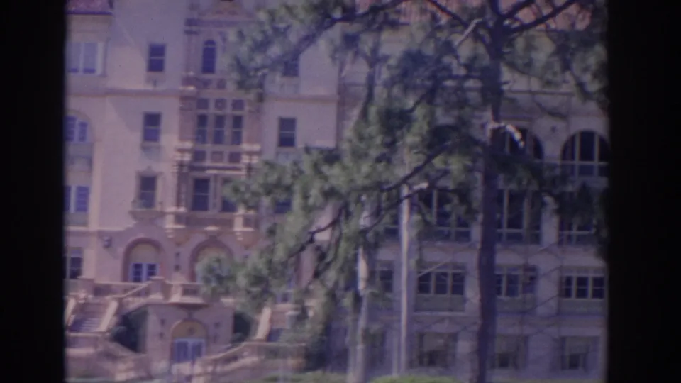 1962 Florida 8mm frame showing a large light-colored building with arched windows, ornamental trim, and pine branches in the foreground.