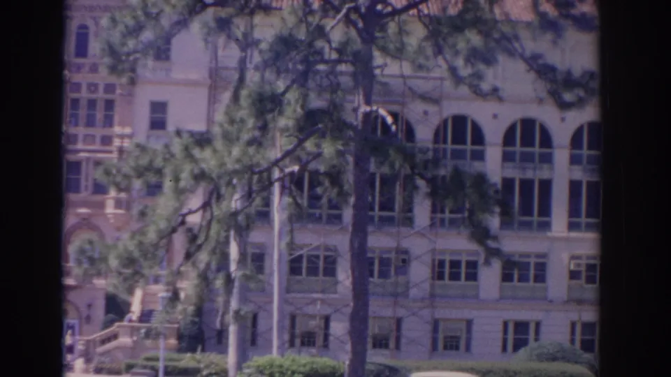 1962 Florida 8mm frame of a large building facade with tall arched windows, smaller window rows, and pine limbs crossing the view.