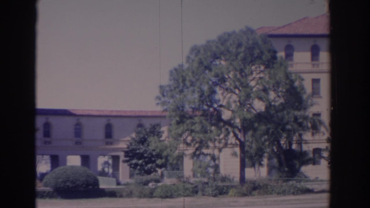 1962 Florida 8mm frame showing a cream institutional-looking building with arched windows, red tile roof, trees, and lawn.