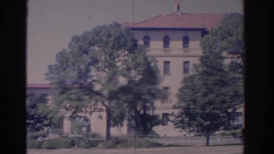 1962 Florida 8mm frame showing the building facade, red roof, lawn, shrubs, and trees during a slow pan.