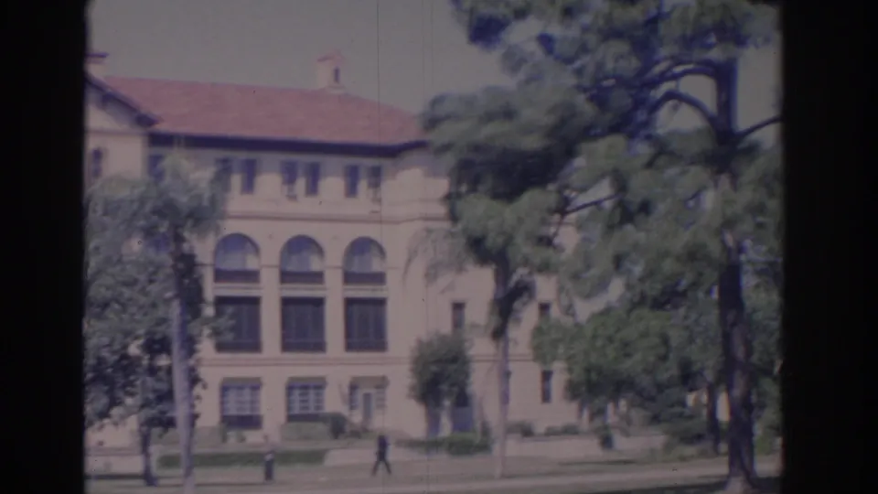 1962 Florida home-movie frame showing a large arched institutional building, red tile roof, trees, lawn, and a distant pedestrian.
