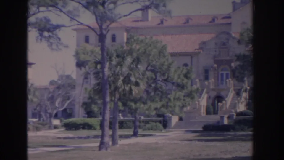 1962 Florida campus exterior with an arched entry, broad staircases, terracotta roof, trees, and manicured grounds.