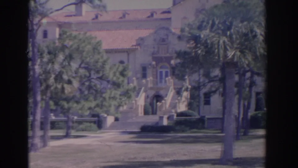 1962 Florida campus view showing a decorative facade, arched doorway, stairs, palms, and shaded grounds on 8mm film.