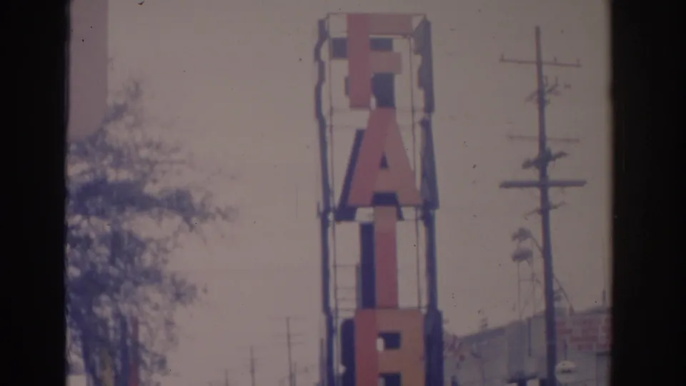 1962 Florida home-movie frame with the vertical FAIR sign in clearer view, utility poles at right, and a roadside building edge below.