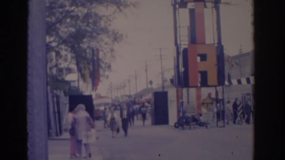 1962 Florida 8mm frame showing people on a waterfront walkway beside a tall colorful structure and distant boats.