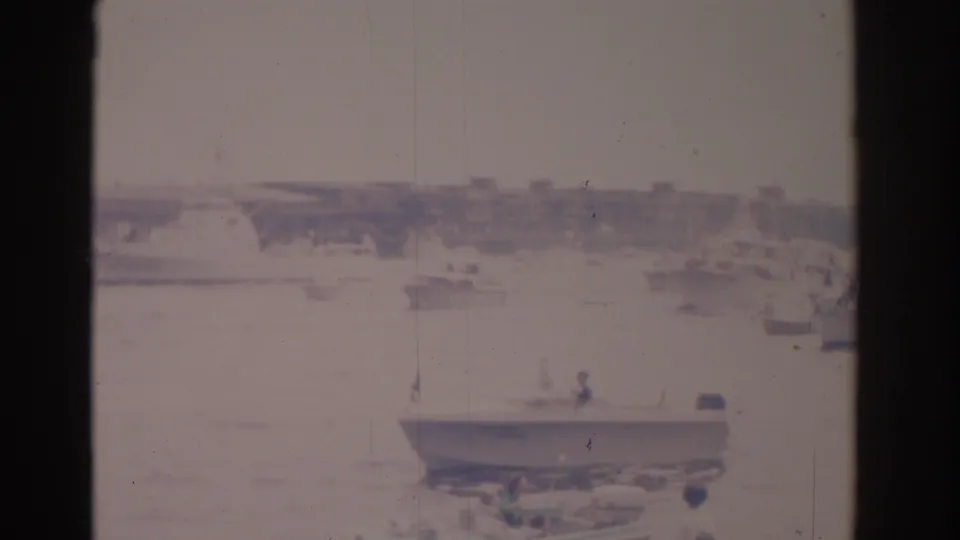 1962 Florida home-movie frame with a sailboat in the foreground and smaller craft scattered across a sunlit harbor.