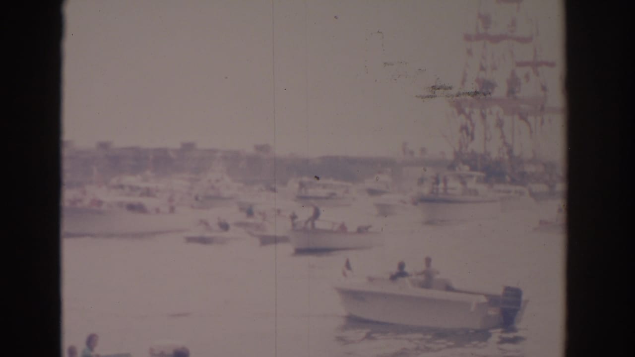1962 Florida harbor scene with small motorboats near a larger decorated ship, seen through soft, faded 8mm home-movie footage.