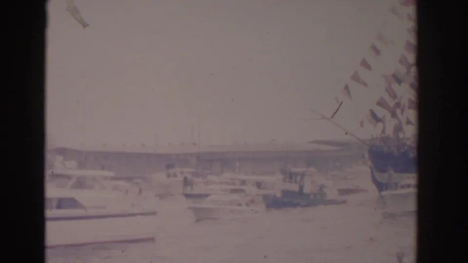 Florida harbor view from 1962 showing pleasure boats, a distant bridge, and red-and-white bunting along the right edge.