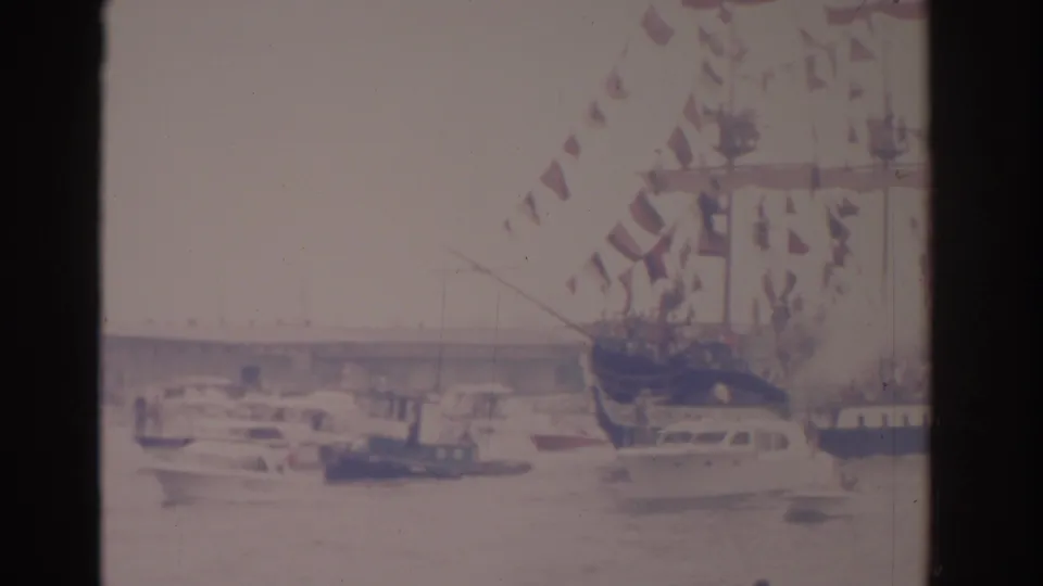 1962 Florida harbor footage shows a pennant-covered ship near small boats, with a bridge and overexposed sky behind it.