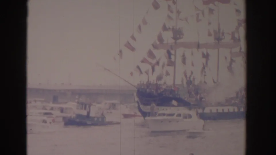 1962 Florida 8mm frame showing a flag-dressed sailing ship in harbor water with small boats nearby.