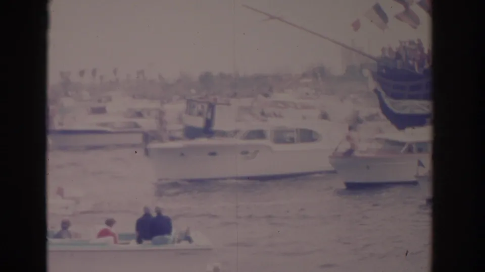 Florida 1962 harbor view with white motorboats, small craft, distant spectators, and part of a flag-decorated sailing vessel.