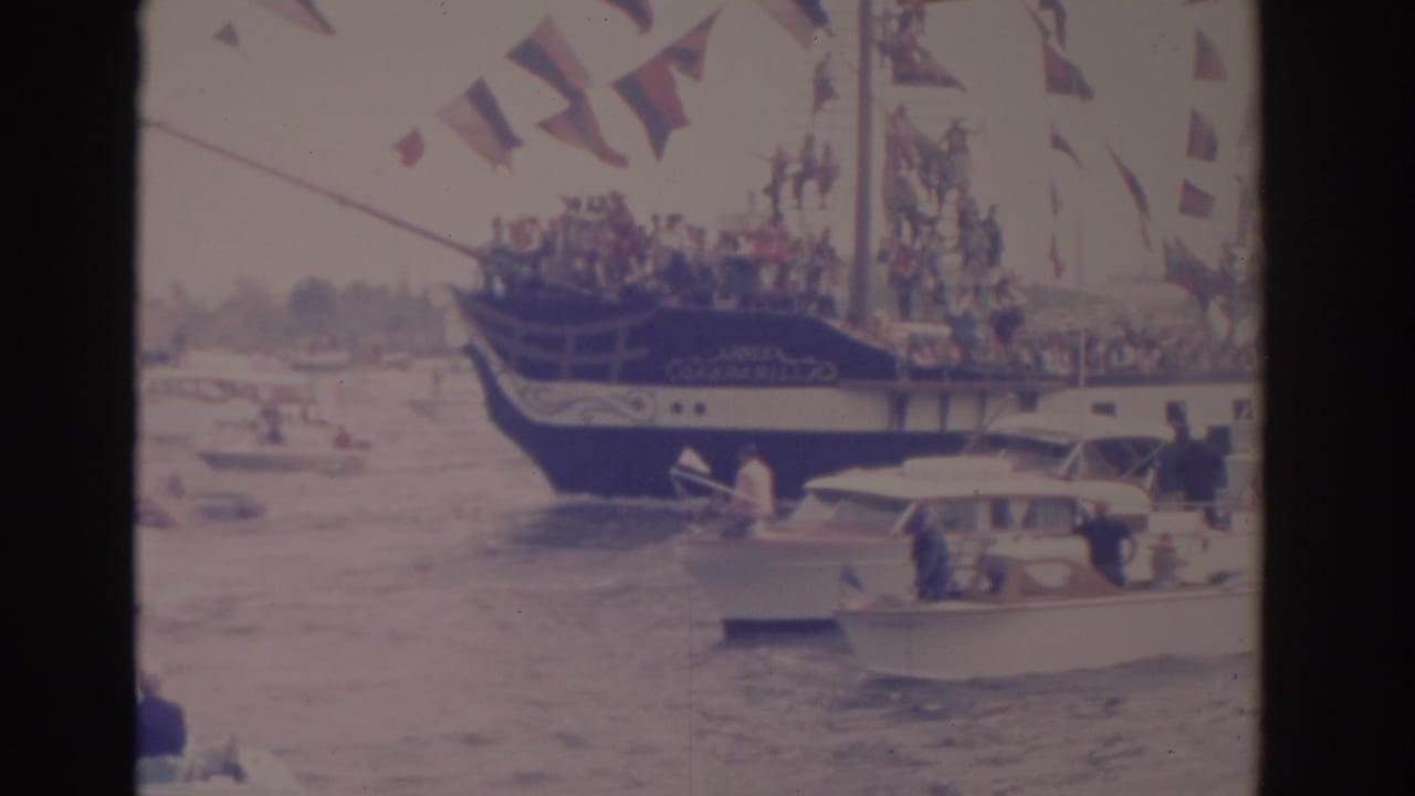 1962 Florida 8mm frame showing a flag-covered parade boat near smaller motorboats with spectators on choppy water.