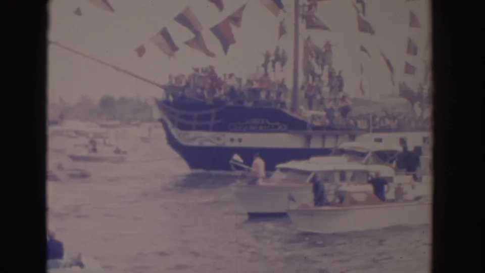 1962 Florida 8mm frame showing a flag-covered parade boat near smaller motorboats with spectators on choppy water.