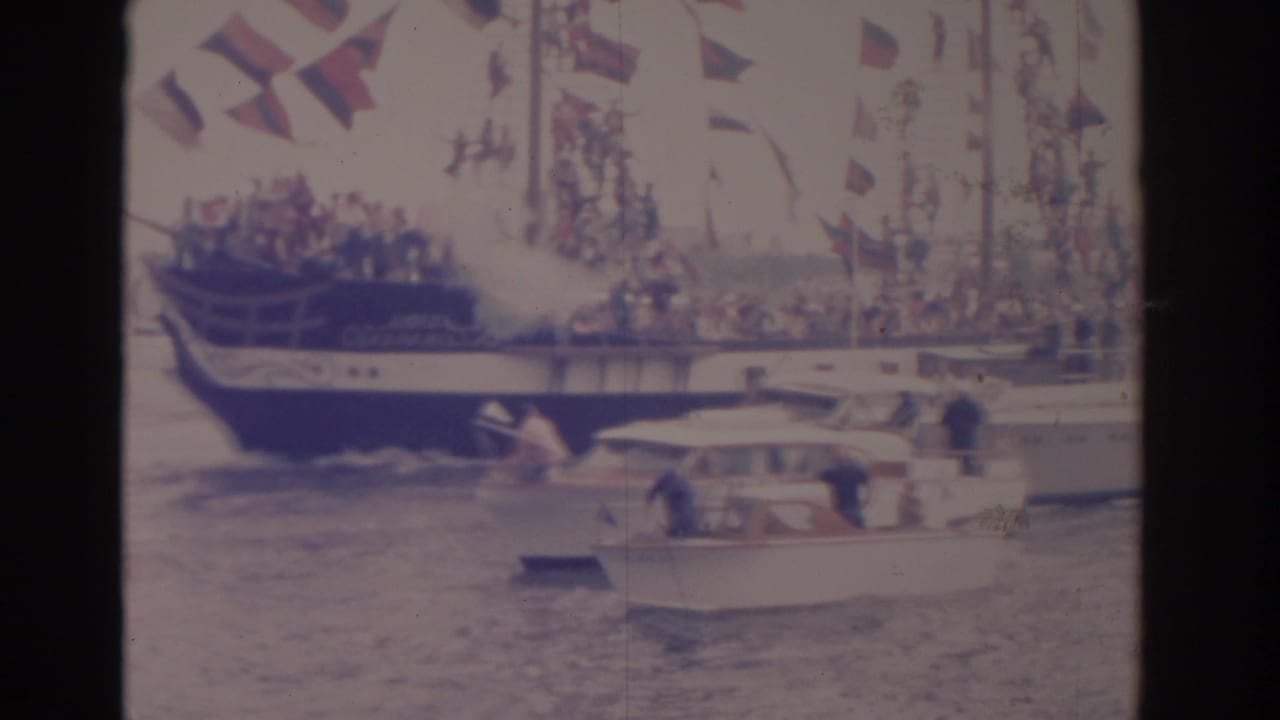 Large flag-covered boat and small motorboat seen from another boat on the water.