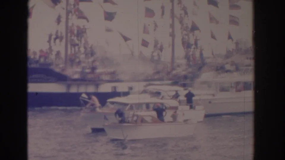 A small motorboat crosses before a larger flag-covered vessel during a 1962 Florida waterfront procession.