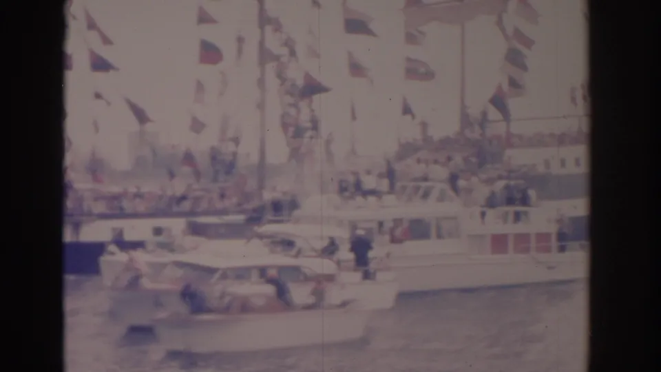 Multiple spectator boats gather beside tall lines of flags in a faded 8mm Florida nautical parade frame.